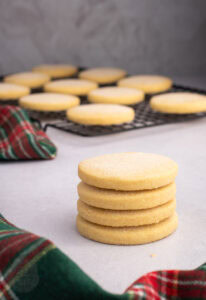 Stack of round Scottish Shortbread biscuits beside more biscuits on a wire cooling rack.