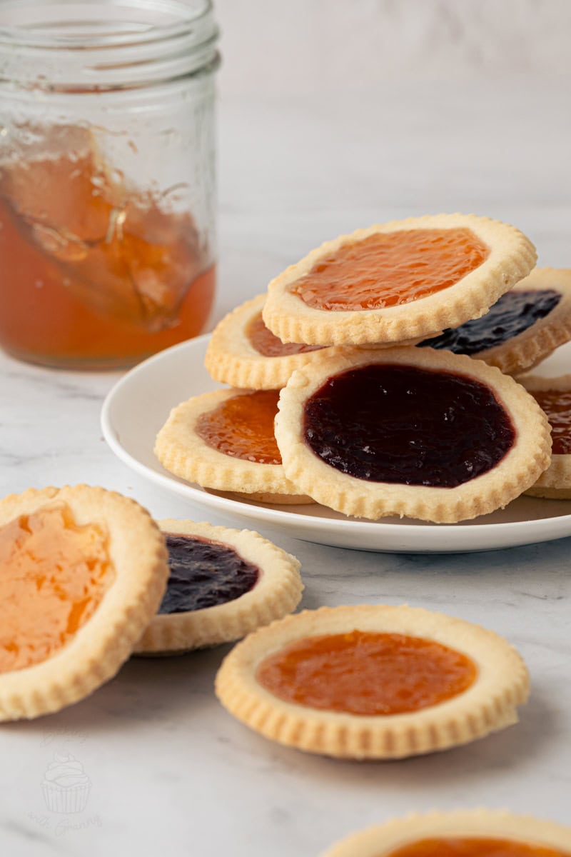 Plate of homemade jam tarts filled with raspberry and apricot jam with a jar of jam in the background