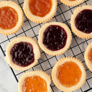 Freshly baked jam tarts with raspberry and apricot filling cooling on a wire rack