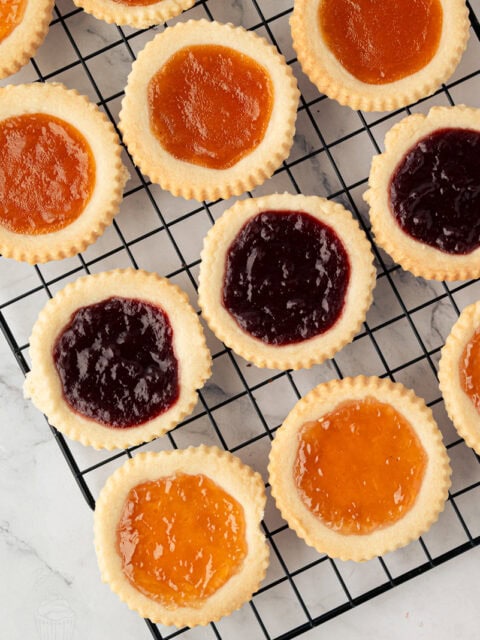 Freshly baked jam tarts with raspberry and apricot filling cooling on a wire rack