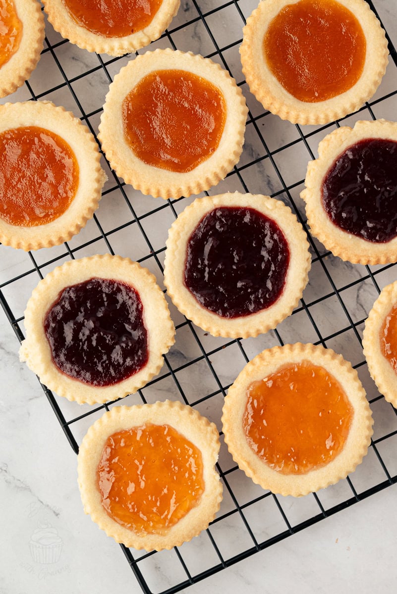 Freshly baked jam tarts with raspberry and apricot filling cooling on a wire rack