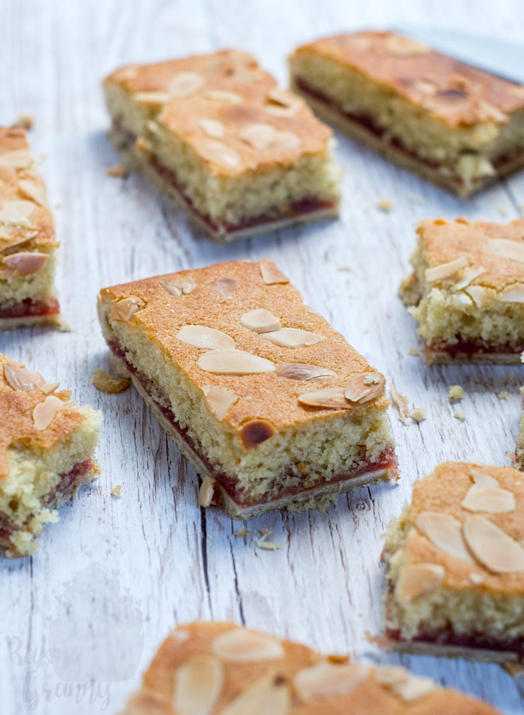Multiple pieces of baked British almond slice tray bake arranged neatly on a light wood surface, highlighted by a golden-brown top crust and scattered almond slices.