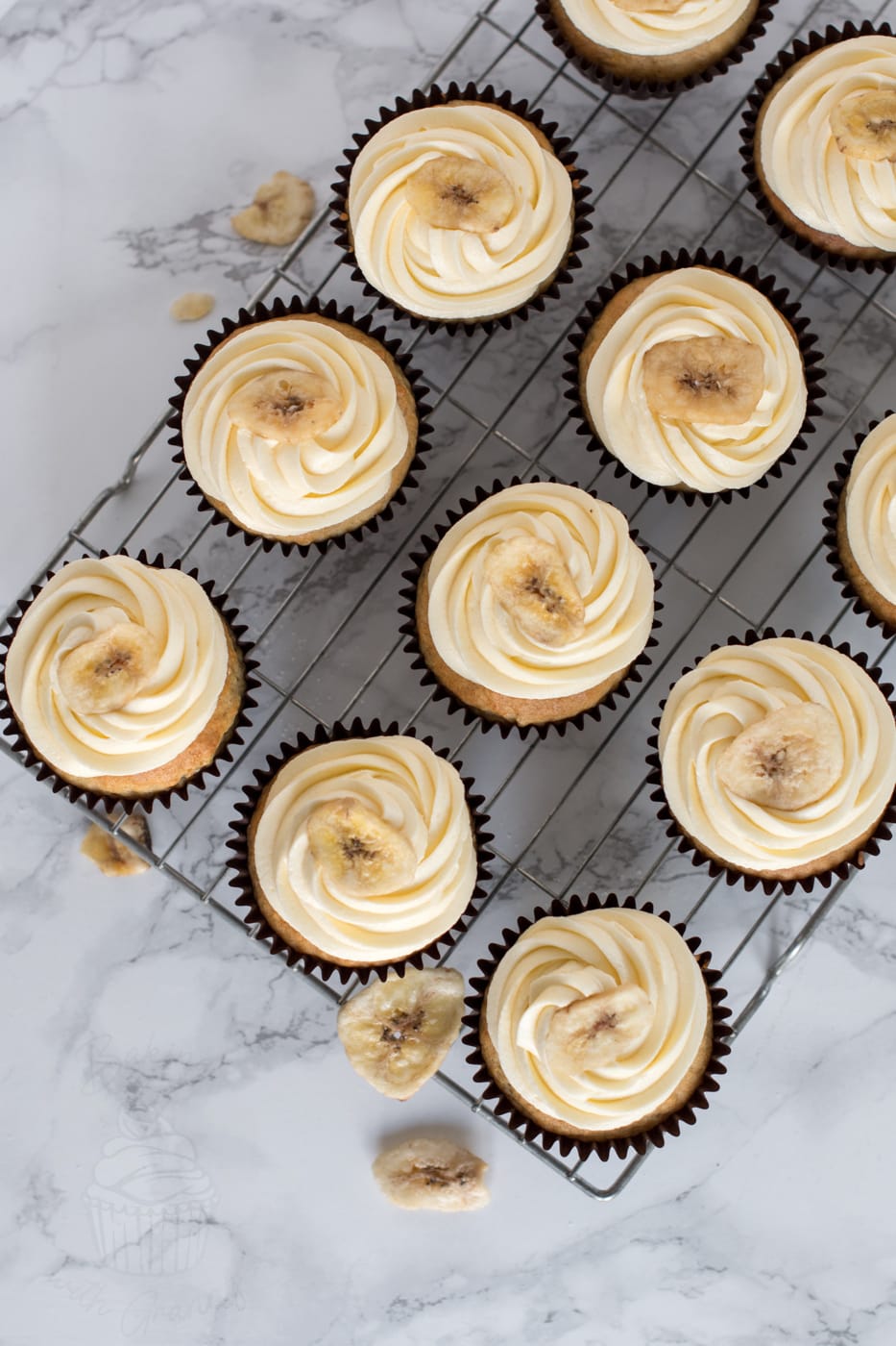 Batch of homemade Banana Cupcakes topped with vanilla buttercream and dried banana chips.