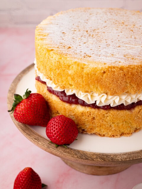 Victoria Sponge filled with strawberry jam and piped buttercream, with fresh strawberries alongside.