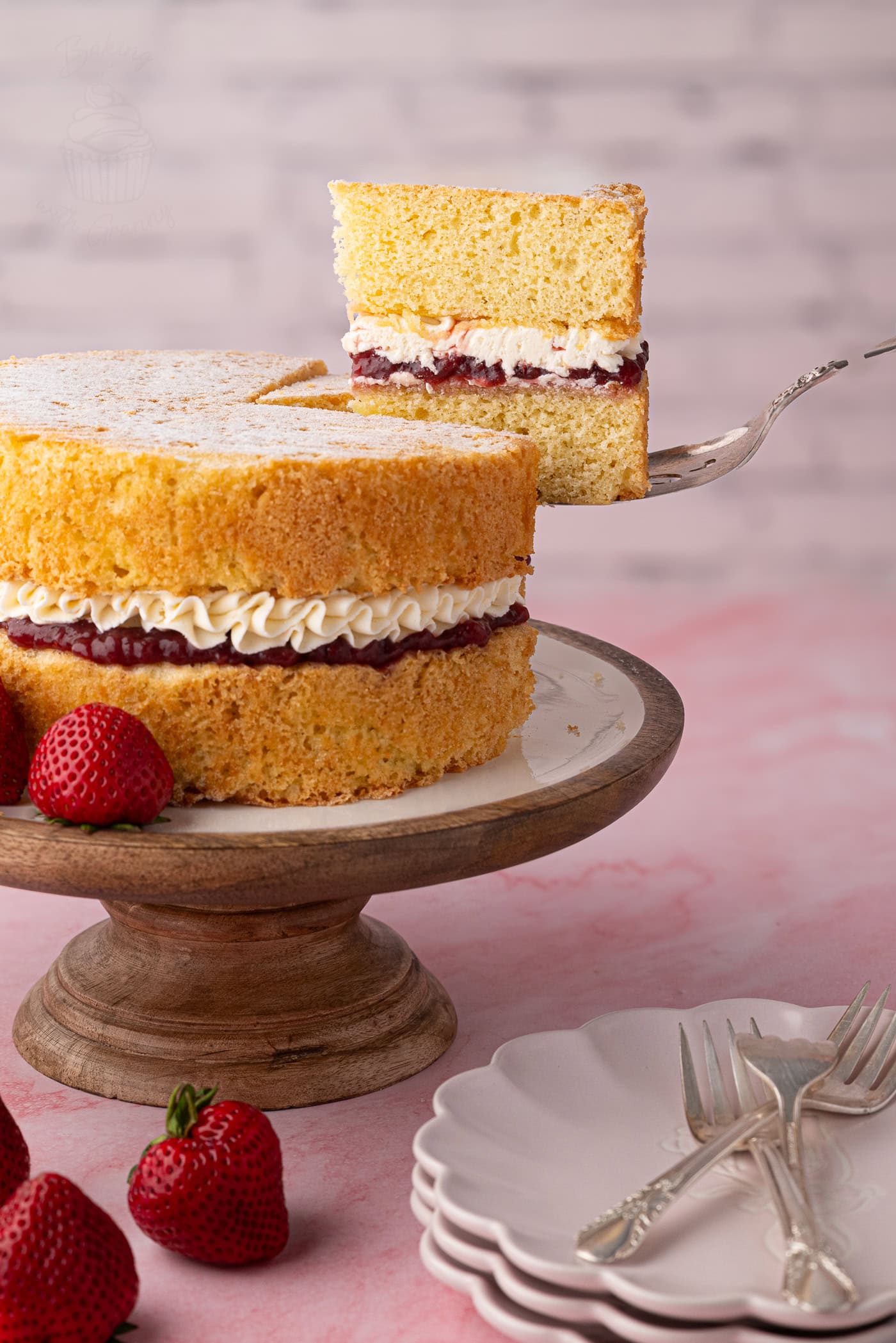 Slice of Victoria Sponge lifted from the cake, showing sponge, strawberry jam and buttercream layers.