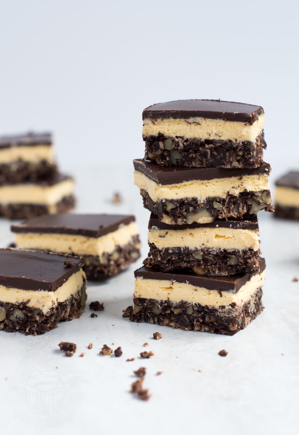 A stack of three-layer Canadian Nanaimo bars surrounded by individual slices on a clean white surface.