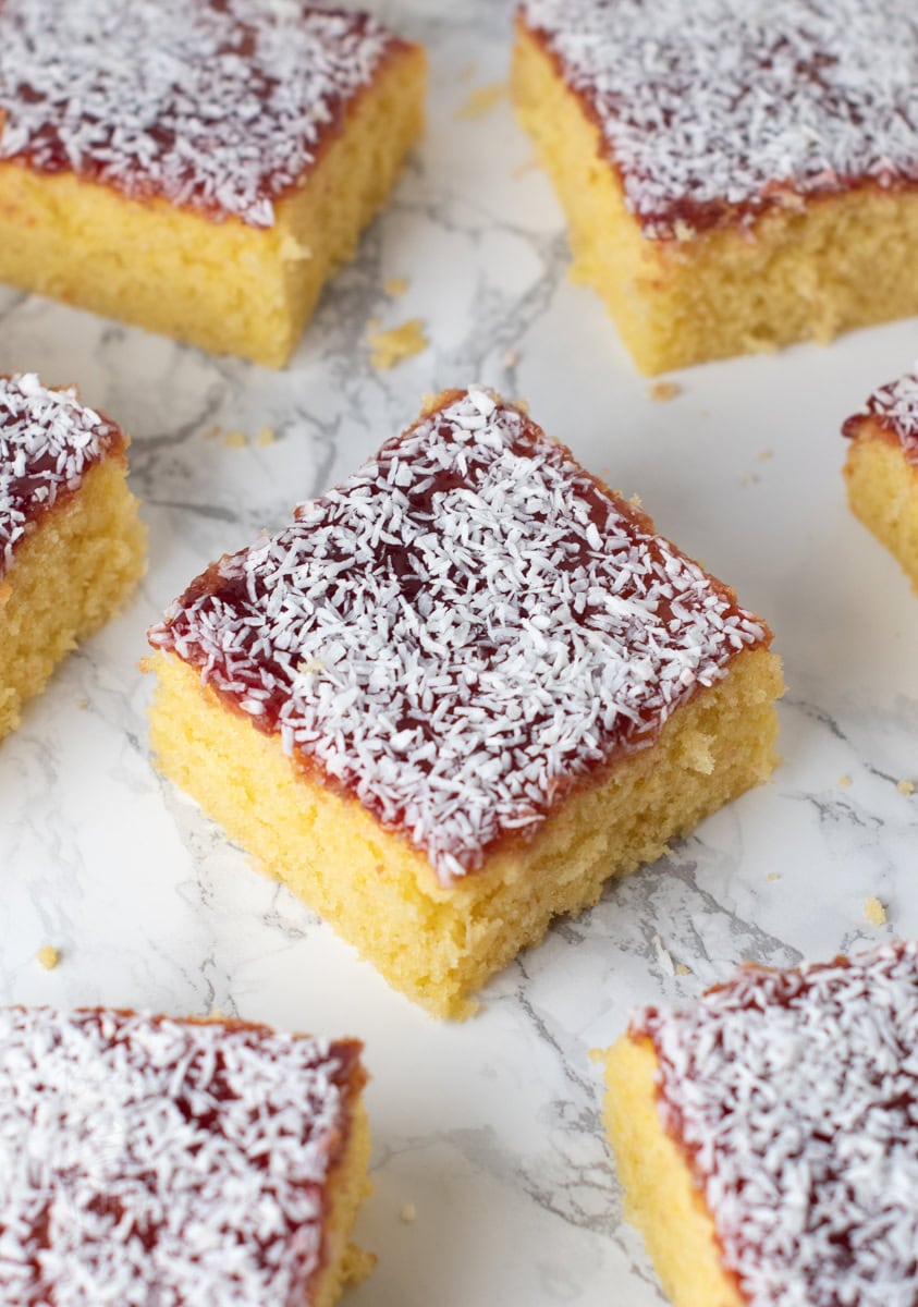 Square slice of jam and coconut school cake topped with raspberry jam and desiccated coconut.