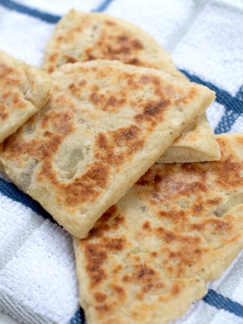 Close view of a small pile of tattie scones. The golden browning on the surface of them can be seen. They are sat on top of a white & blue chequered tea towel.