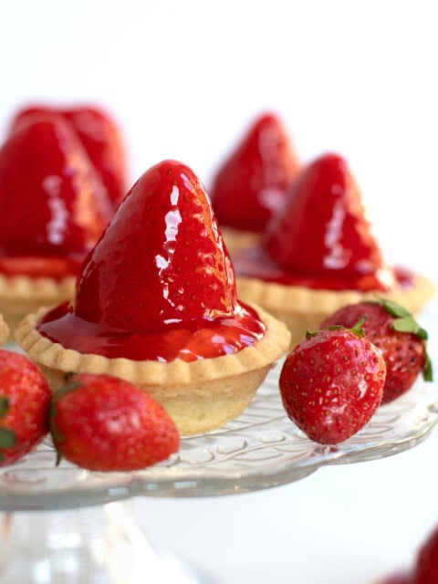 Scottish strawberry tarts, sat on a glass stand, with strawberries placed around.