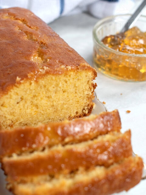 Marmalade cake loaf, sliced into individual portions, with a small jar of open marmalade in the background.