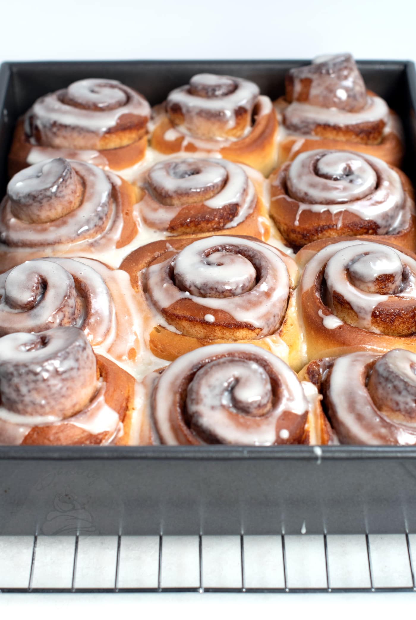 Cinnamon Rolls in a tin, with sticky white icing on top, showing the cinnamon sugar filled swirls.