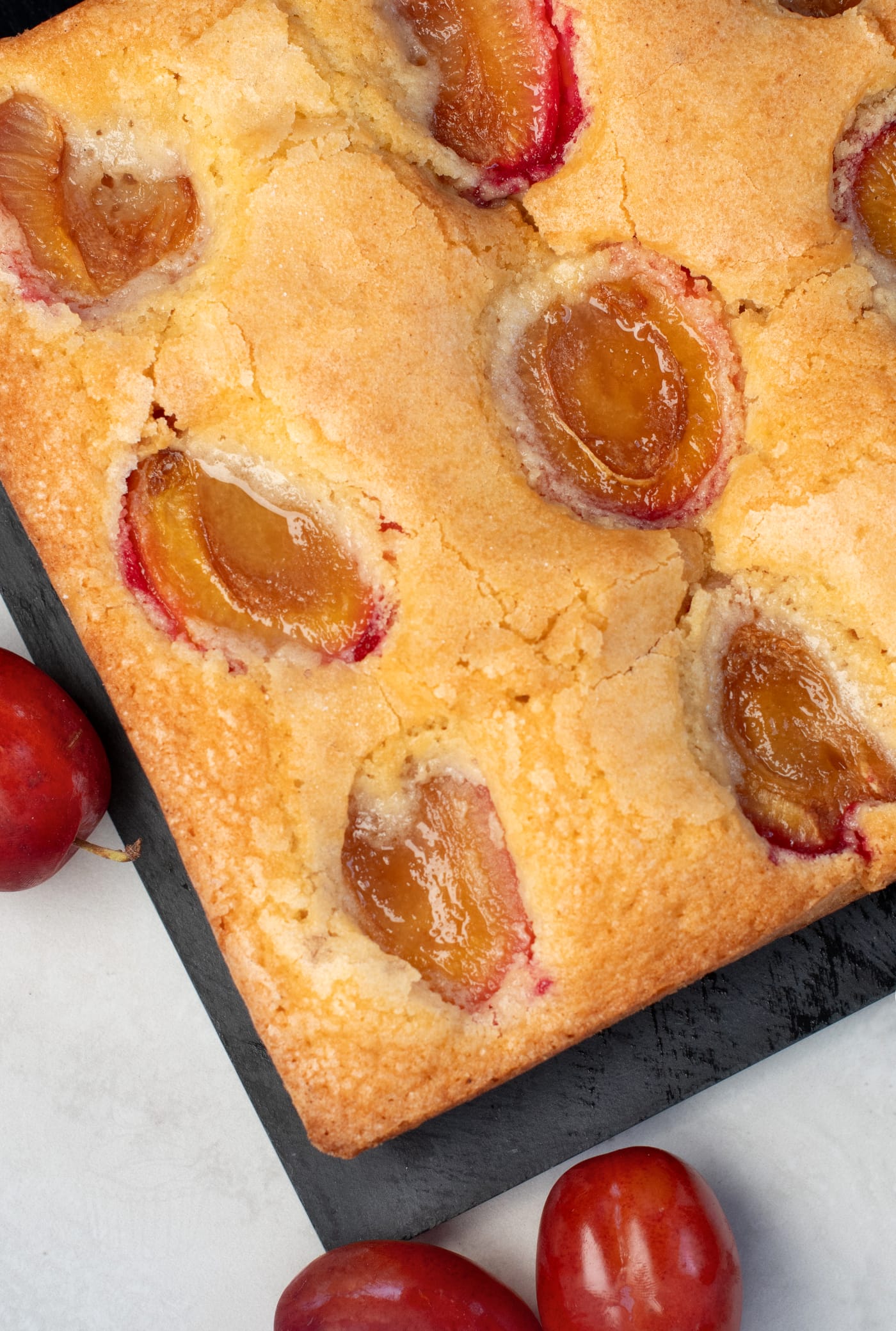 Square plum cake with baked plum halves and a golden sugar-topped surface.
