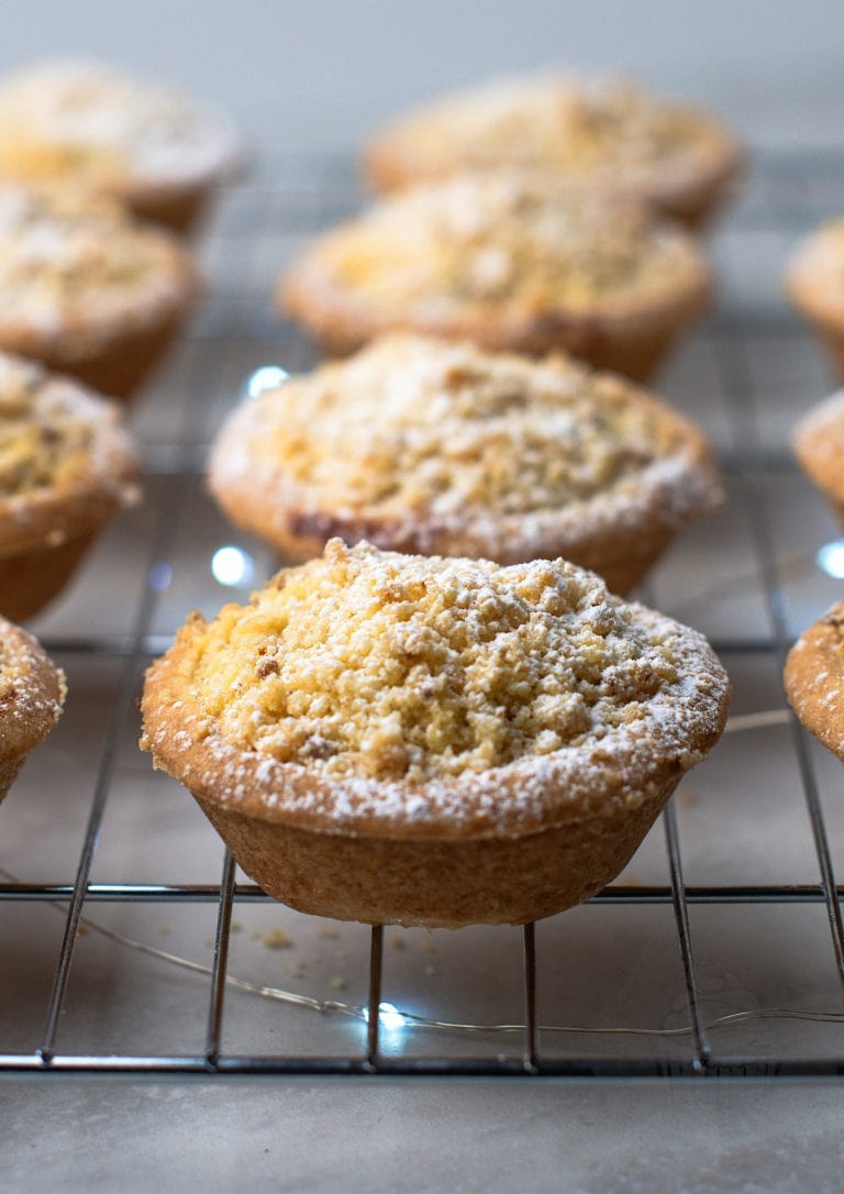 Crumble Top Mince Pies recipe from Baking with Granny. Delicious classic shortcrust mince pie, with a crumble topping, sat on top of a cooling rack, with Christmas lights twinkling underneath.
