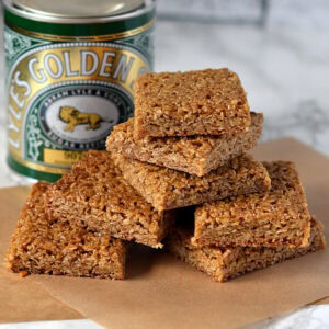 Stack of golden-brown flapjack squares beside a tin of Lyle’s Golden Syrup.