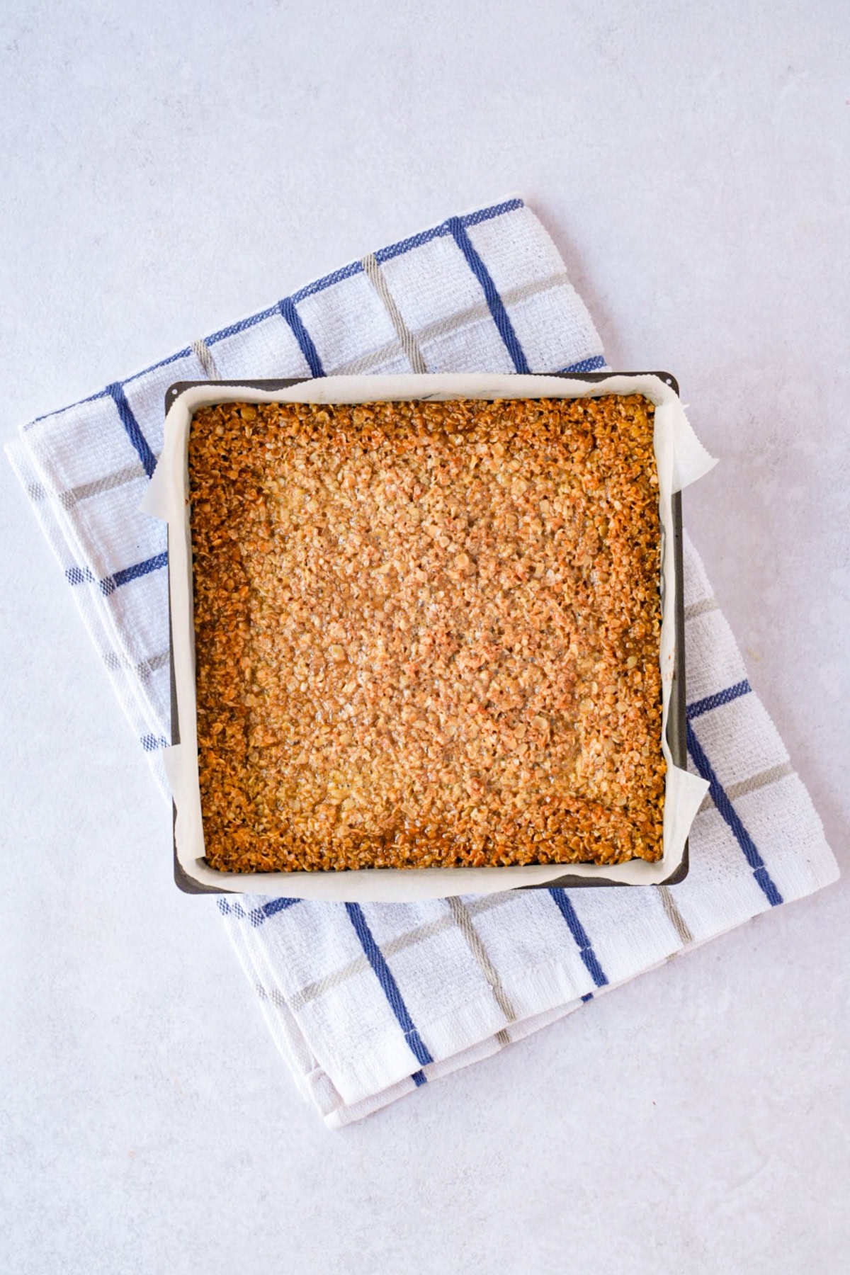 Baked Flapjack in a lined square tin with lightly golden edges.
