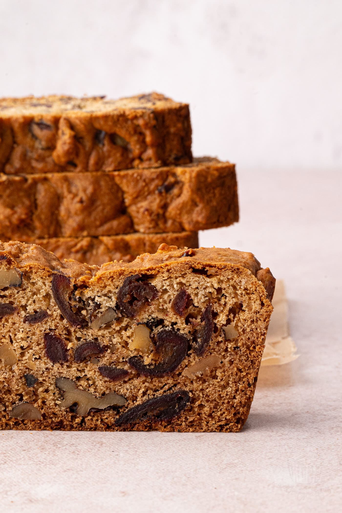 Slices of Date and Walnut Cake stacked on a light surface, showing a cross-section of the inside of the cake.