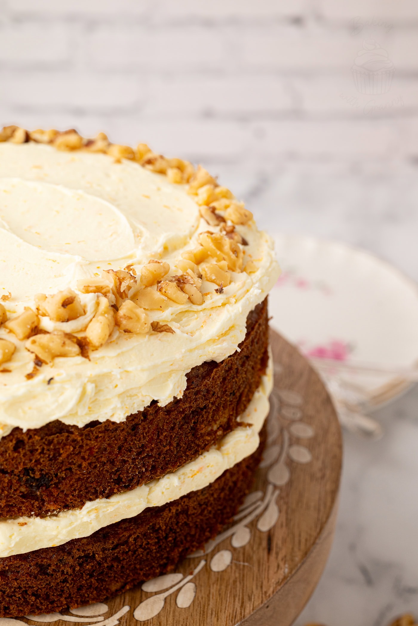 Close-up of the top edge of a carrot cake, showing the buttercream and a ring of chopped walnuts.