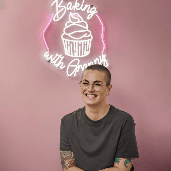 Amy Beth Reid pictured against a pink wall with a LED light of the Baking with Granny logo behind her.