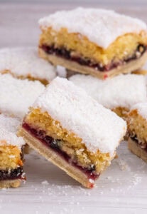 Scottish Snow Cake slices stacked on a white surface, showing the jam and sponge layers beneath a dusting of coconut.