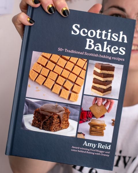 Amy Reid smiling and holding a copy of her debut self-published cookbook, Scottish Bakes.