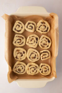 Unbaked Chelsea Buns arranged in a lined baking dish before their second rise.