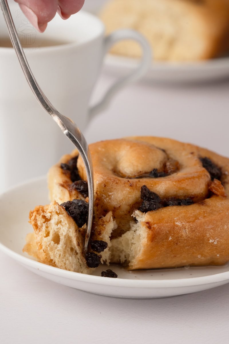 Fork pulling apart a soft and fluffy homemade Chelsea Bun filled with currants and sultanas.