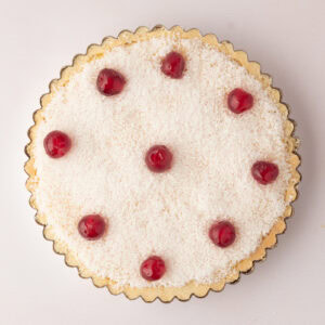 Top-down view of a traditional Manchester Tart in a fluted tart tin topped with coconut and glace cherries.