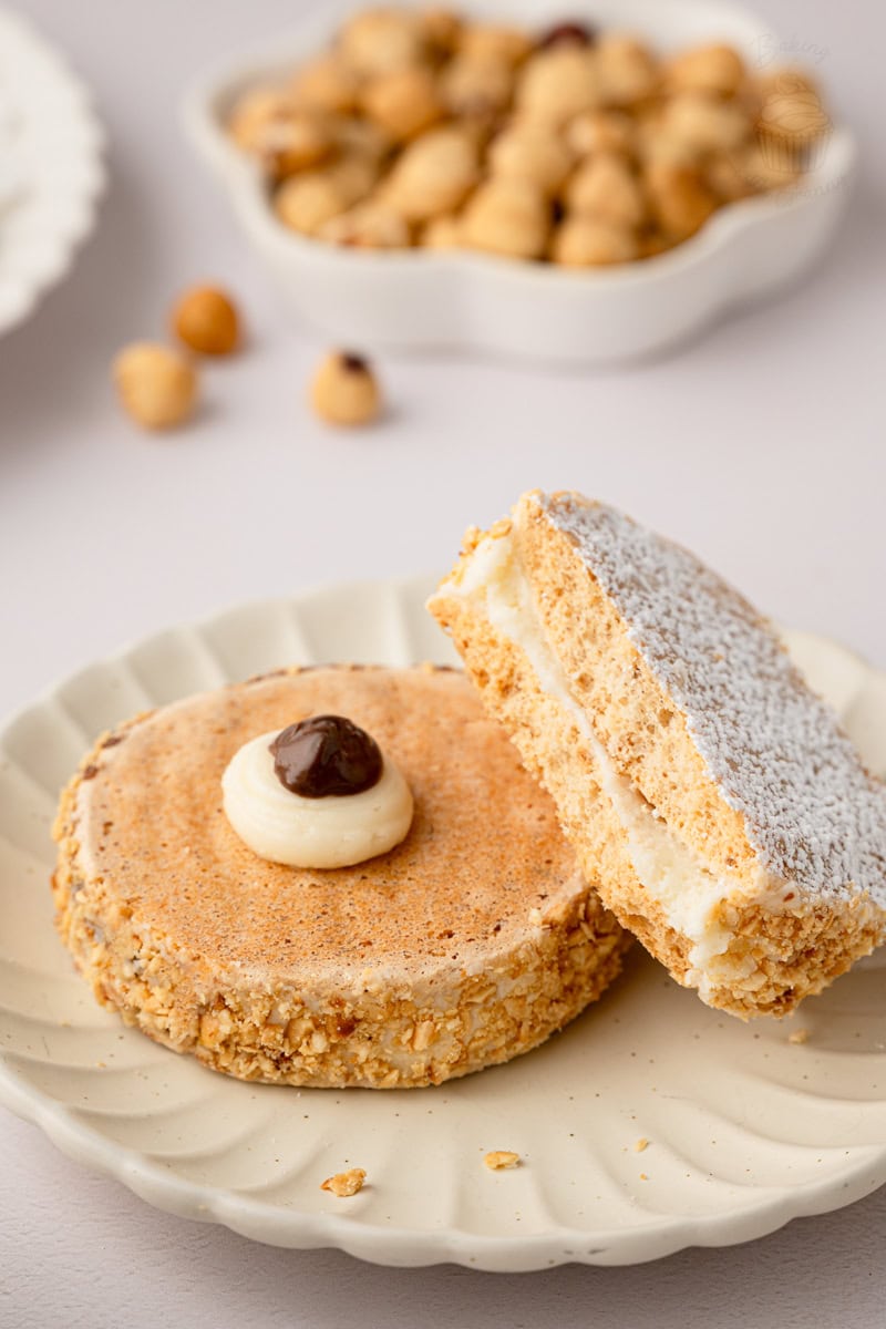 Close-up macro shot of a halved hazelnut meringue sandwich biscuit on a fluted plate, showing the airy texture of the meringue shell and smooth buttercream centre.
