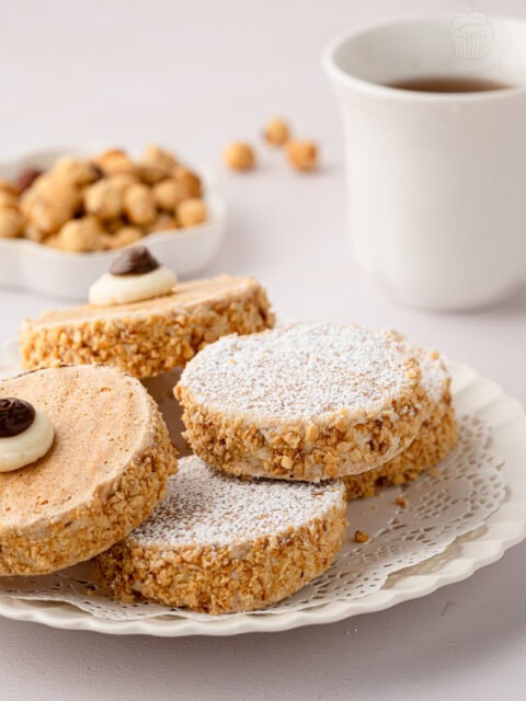 Eye-level close-up of a stacked pile of icing-sugar-dusted Japonaise cakes on a white plate with a vintage lace doily.