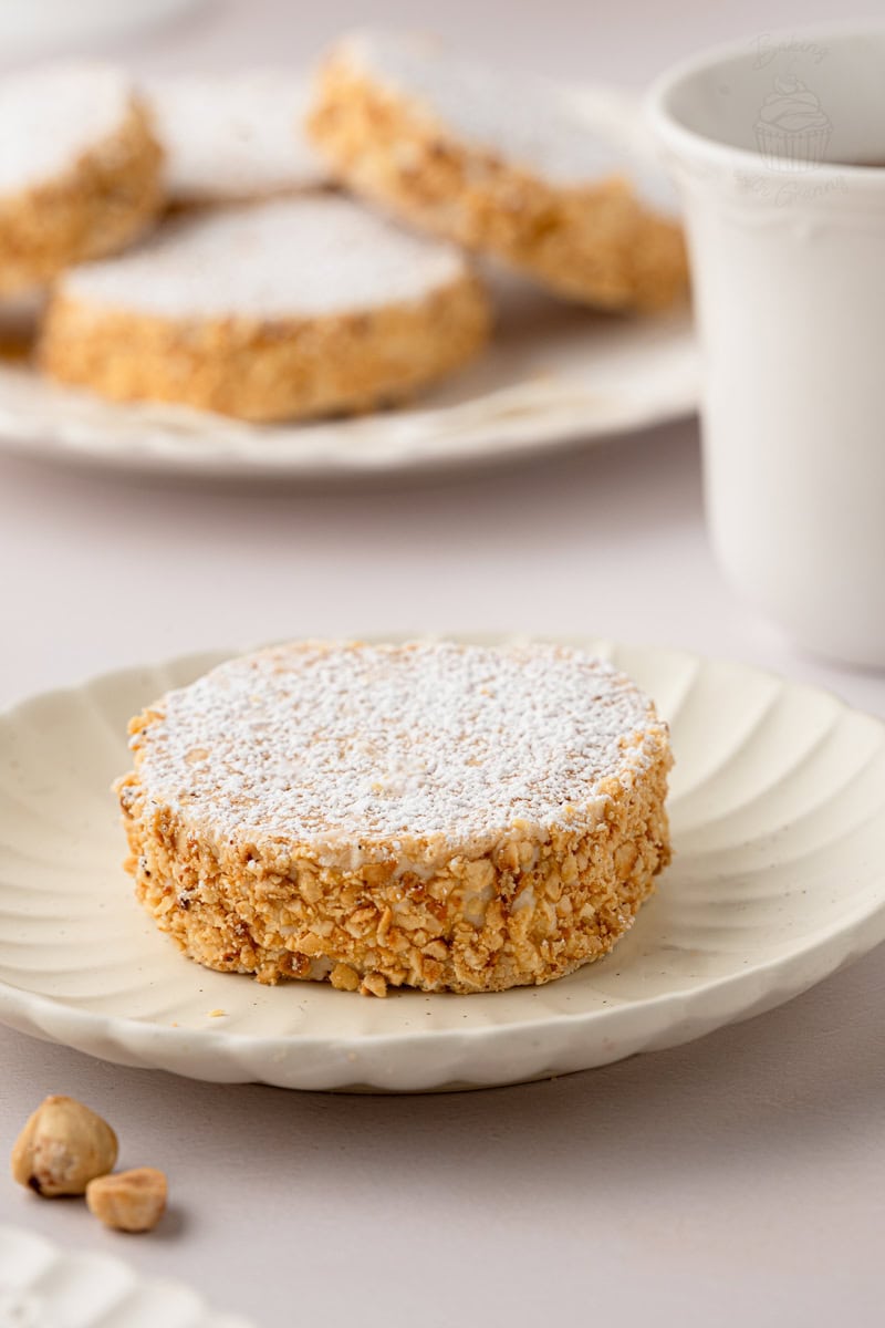 Single traditional Scottish Japonaise biscuit dusted generously with powdered sugar, served individually on a small fluted ceramic plate.