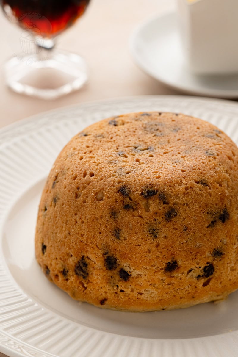 Close-up of a whole traditional British Spotted Dick pudding showing the suet sponge texture and scattered currents.