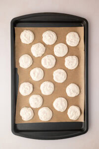 Raw hazelnut meringue mixture piped into neat circles on a baking sheet lined with brown parchment paper before going into the oven.