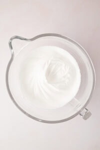 Thick, glossy white egg whites whipped to stiff peaks in a glass mixing bowl, ready for making traditional Scottish Japs biscuits.