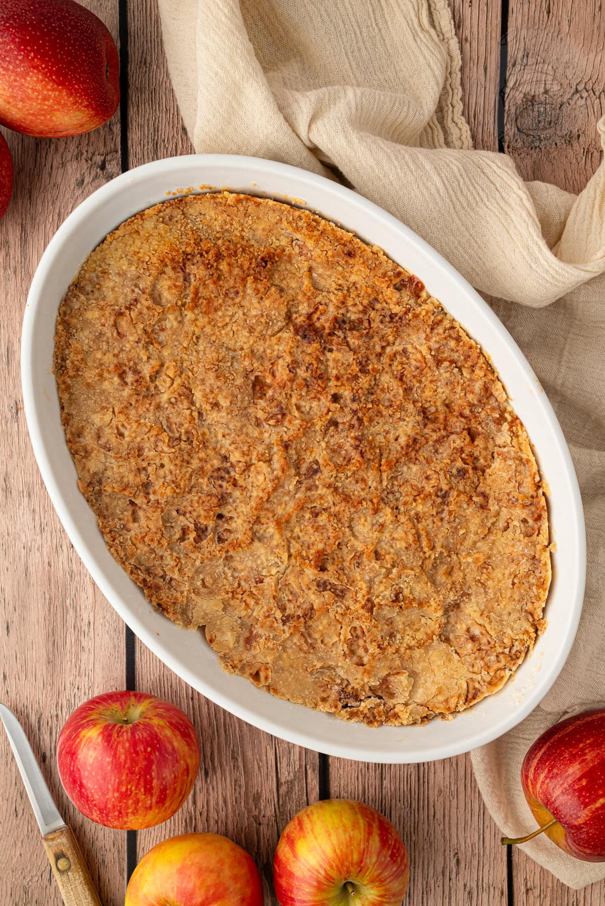 Baked apple crumble in a white dish with red apples beside it.