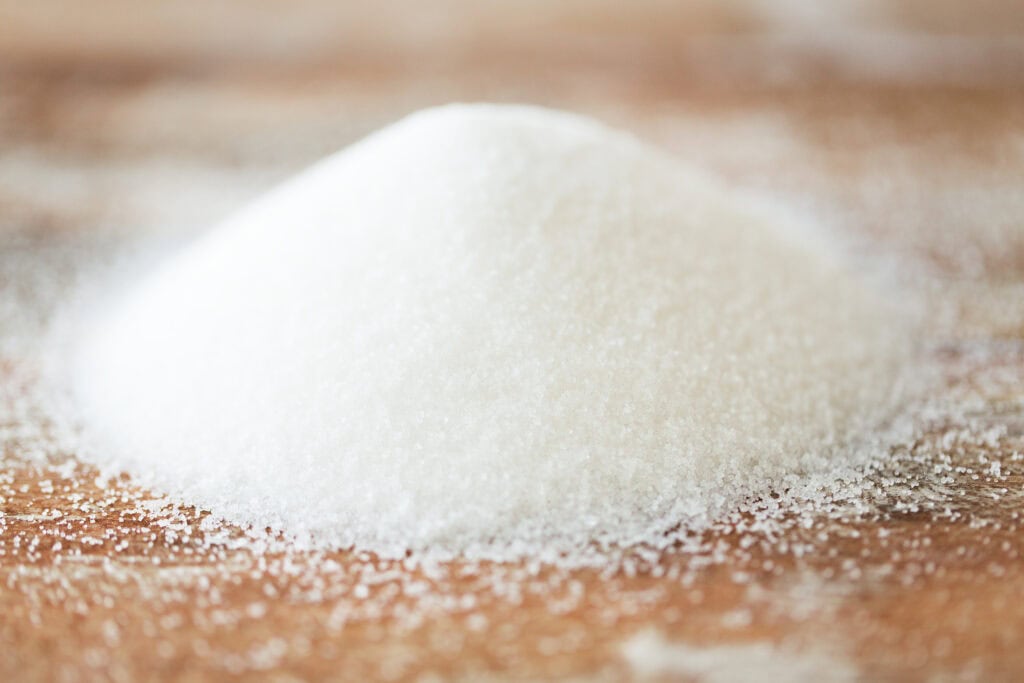 A pile of caster sugar crystals on a light wooden surface.