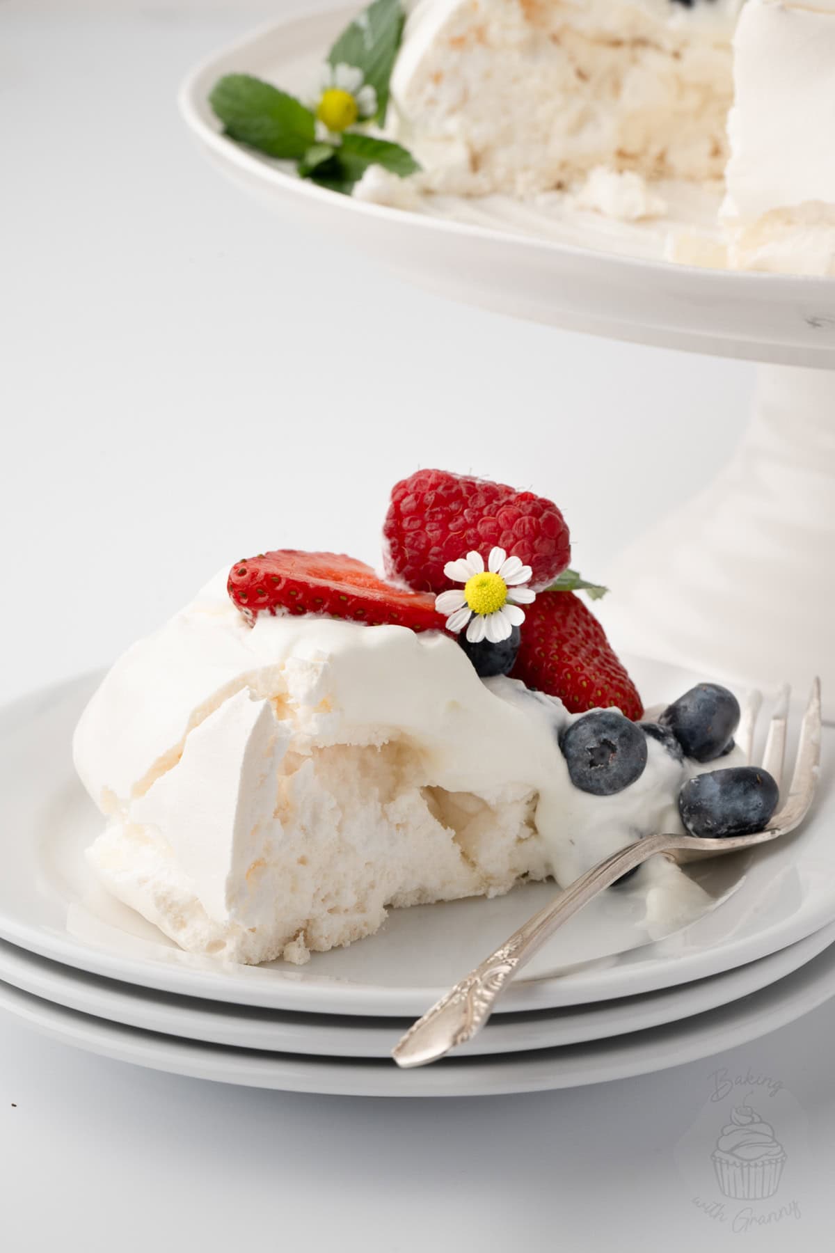 Slice of Pavlova on a plate showing the white meringue centre beneath cream and fresh berries.