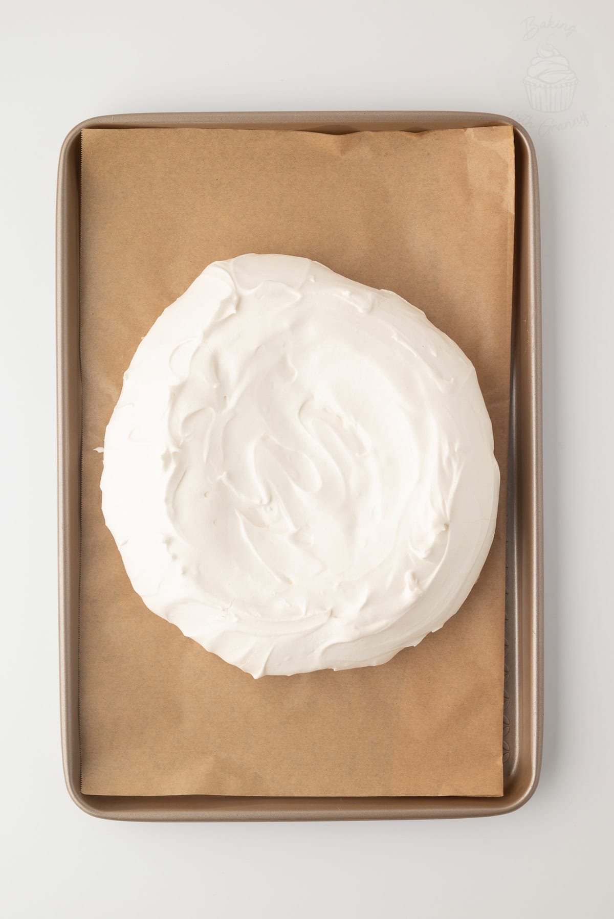 Baked Pavlova meringue on a lined tray with a pale, dry surface and small cracks.