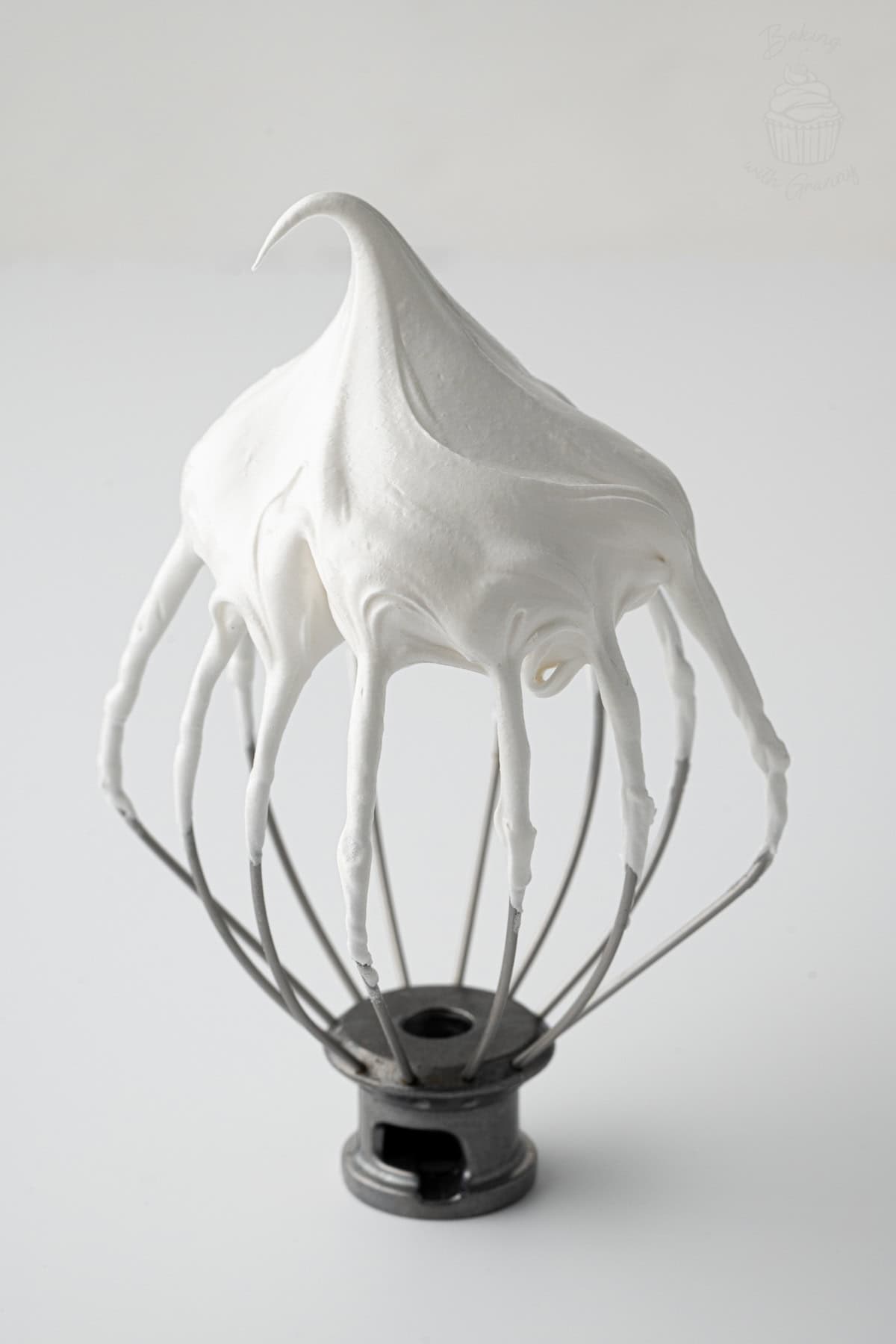 Whisk attachment coated in glossy Pavlova meringue holding a stiff peak.