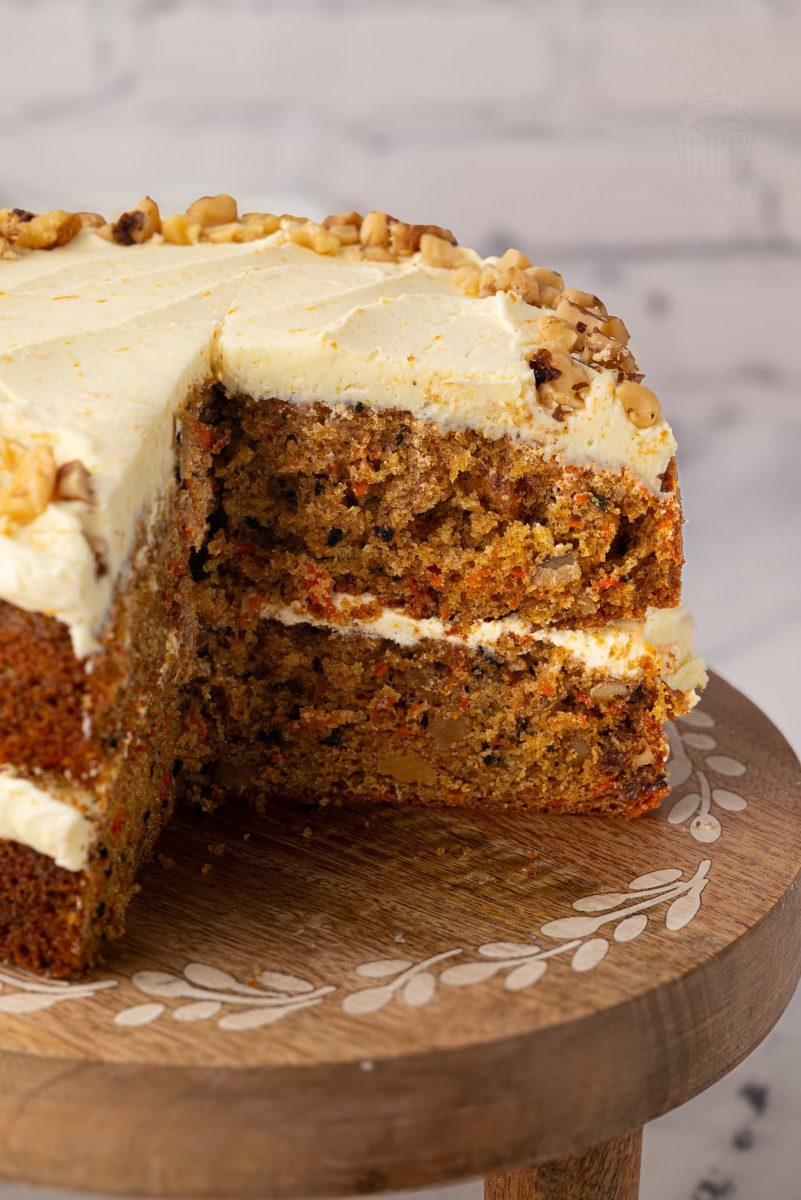 Close-up of the inside of a carrot cake, showing its soft texture and chunks of walnut and carrot, with buttercream between the layers and on top.