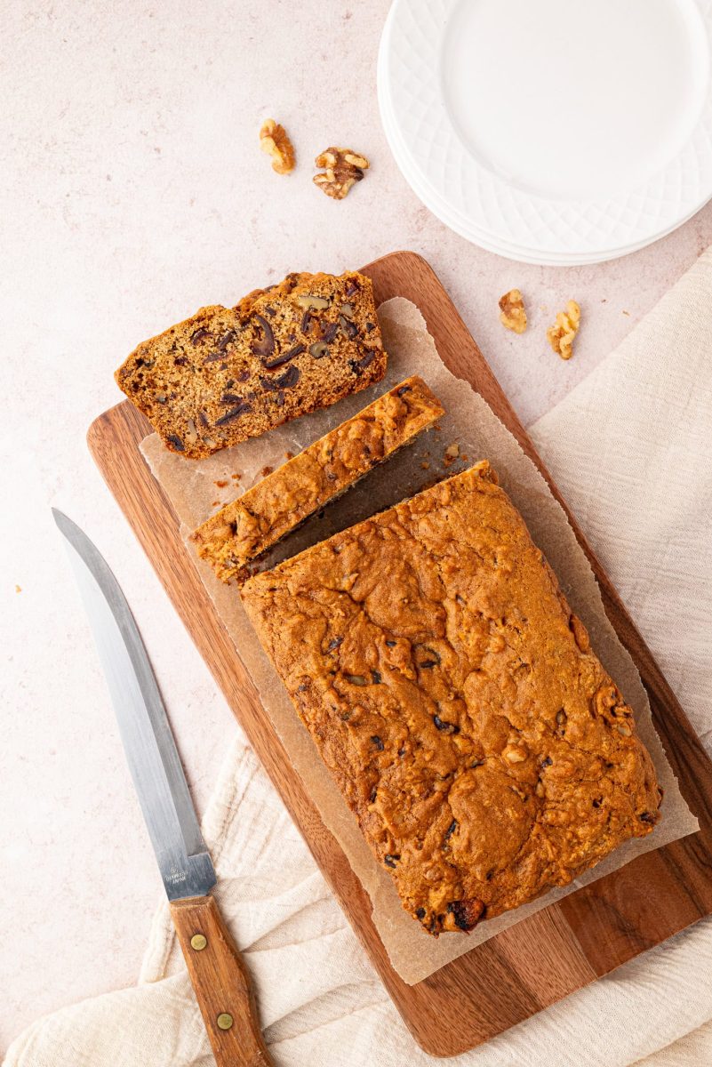 Date and walnut loaf on a wooden cutting board with two slices cut and a knife beside.